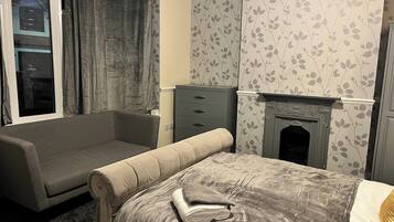 A bedroom with a bed, a sofa, a dresser, and a fireplace.
