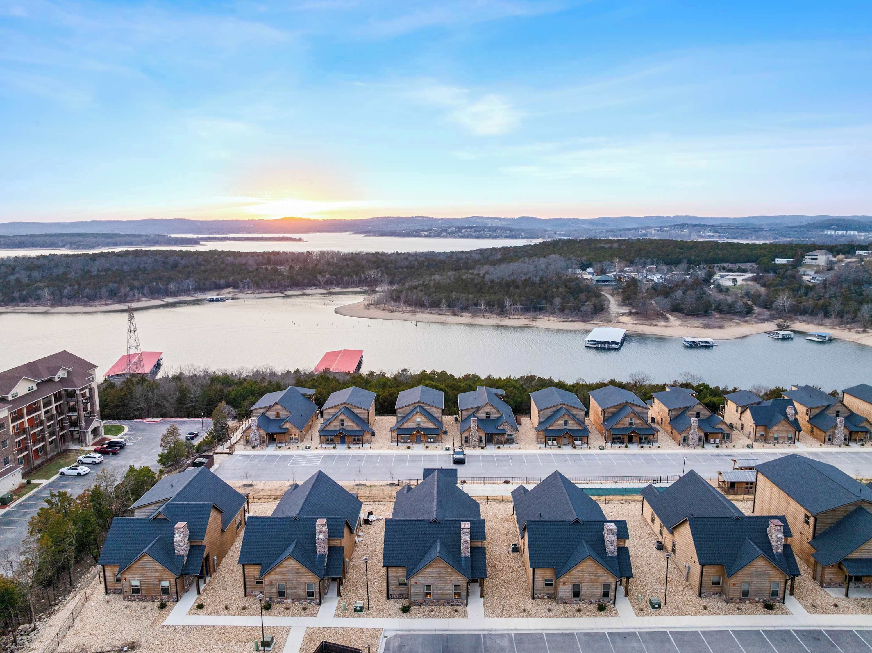 A residential area with multiple houses, a parking lot, and a body of water in the background.