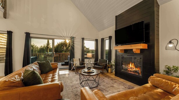 A modern living room with leather sofas, a fireplace, a TV, and a balcony with curtains. - Fire Pit! Hot Tub! Stunning Views! Two Fireplaces! (Branson)