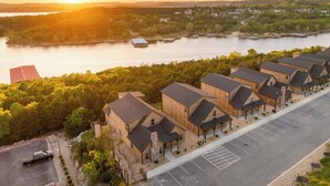 A row of log cabin-style buildings with a parking lot and a view of a lake at sunset. - Fire Pit! Hot Tub! Stunning Views! Two Fireplaces! (Branson)