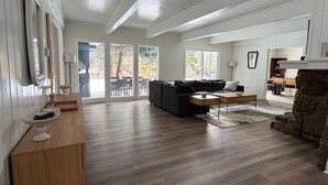 Un salón amplio con piso de madera, un sofá oscuro, una mesa de centro de madera y una chimenea de piedra.