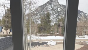 Vista a través de una ventana que muestra un edificio con escaleras, una montaña cubierta de nieve y un área pavimentada con rocas.