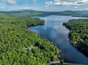 An aerial view of a lake surrounded by dense forest, with a few houses and boats visible. - Indian Pond Cabin (Wilson Pond Cabin) (Greenville)
