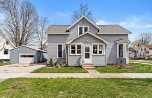 A two-story residential house with a garage, a front porch, and a small front yard. - Experience charm at the Historic Emily Filer Home in Ludington (Ludington)