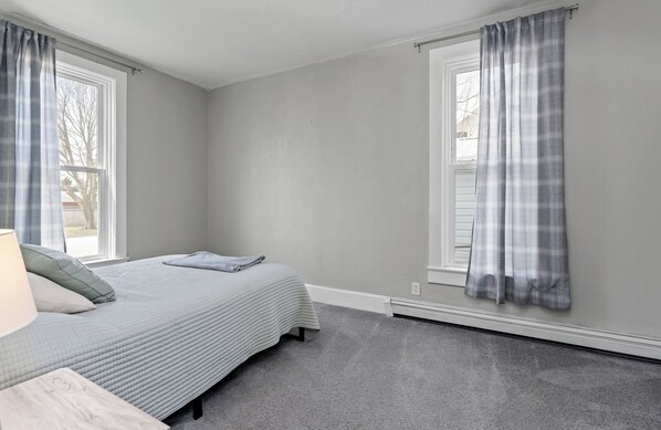 A bedroom with a bed, a nightstand, a window, and a door. - Experience charm at the Historic Emily Filer Home in Ludington (Ludington)
