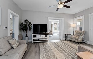 A living room with a TV, sofa, armchair, and a ceiling fan.
