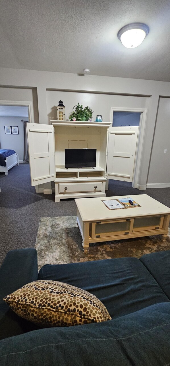 A living room with a television on a white stand, a coffee table, a blue sofa, and a leopard print pillow.