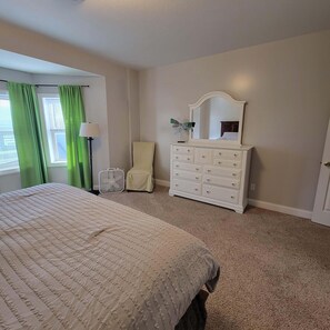 Une chambre à coucher avec un grand lit, une commode avec un miroir, une chaise et une lampe sur pied.