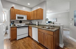 A kitchen with wooden cabinets, a microwave, stove, dishwasher, and a sink. - Ludington STRAM - Unit 202, a cozy 2-bedroom retreat (Ludington)