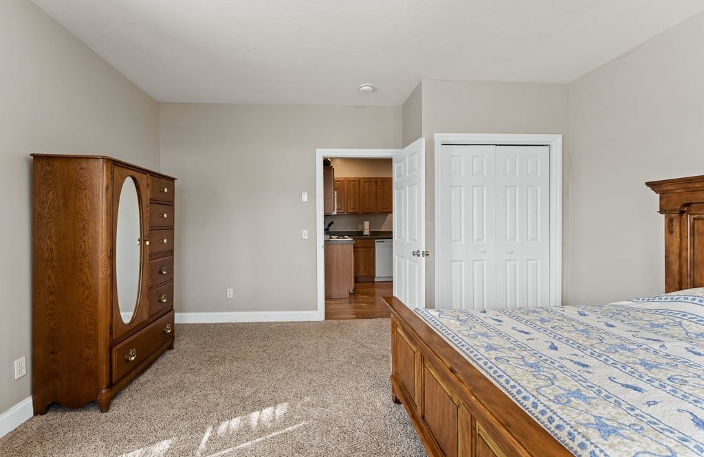 Une chambre à coucher comprenant un lit, une commode et une porte donnant sur la cuisine.