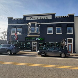 Un bâtiment à deux étages, doté d’une façade noire et blanche, d’une enseigne bien visible « Wm Stram » au-dessus de l’entrée, et d’une vitrine portant l’inscription « Ludington Hobbies » avec un logo vert.
