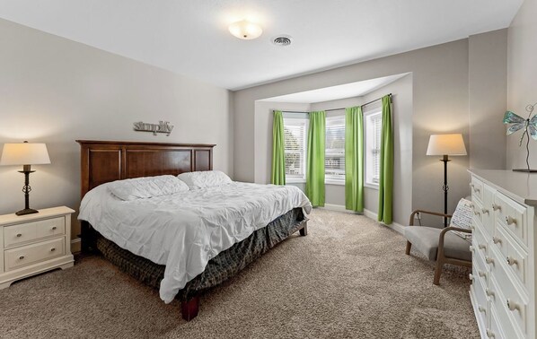 A bedroom with a bed, a nightstand, a dresser, a chair, and a window with curtains. - Ludington STRAM - Unit 202, a cozy 2-bedroom retreat (Ludington)