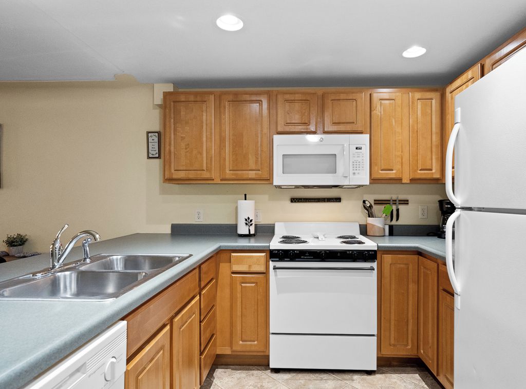 A kitchen with wooden cabinets, a white stove, a microwave, and a refrigerator.