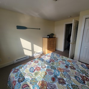 A bedroom with a bed, a dresser, a door, and a wall-mounted paddle. - Downtown condo in Ludington, perfect for a cozy getaway! (Ludington)