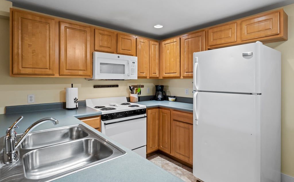A kitchen with wooden cabinets, a white refrigerator, a microwave, a stove, and a sink.