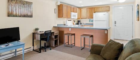 A compact living space with a kitchenette, a television, a sofa, and a painting on the wall.