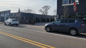 A street with two cars parked on the side, a building with a sign that reads "North Pointe Real Estate," and a tree in the background.