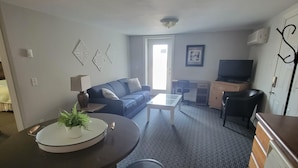 A living room with a sofa, coffee table, and a TV. There is a dining area with a table and chairs.