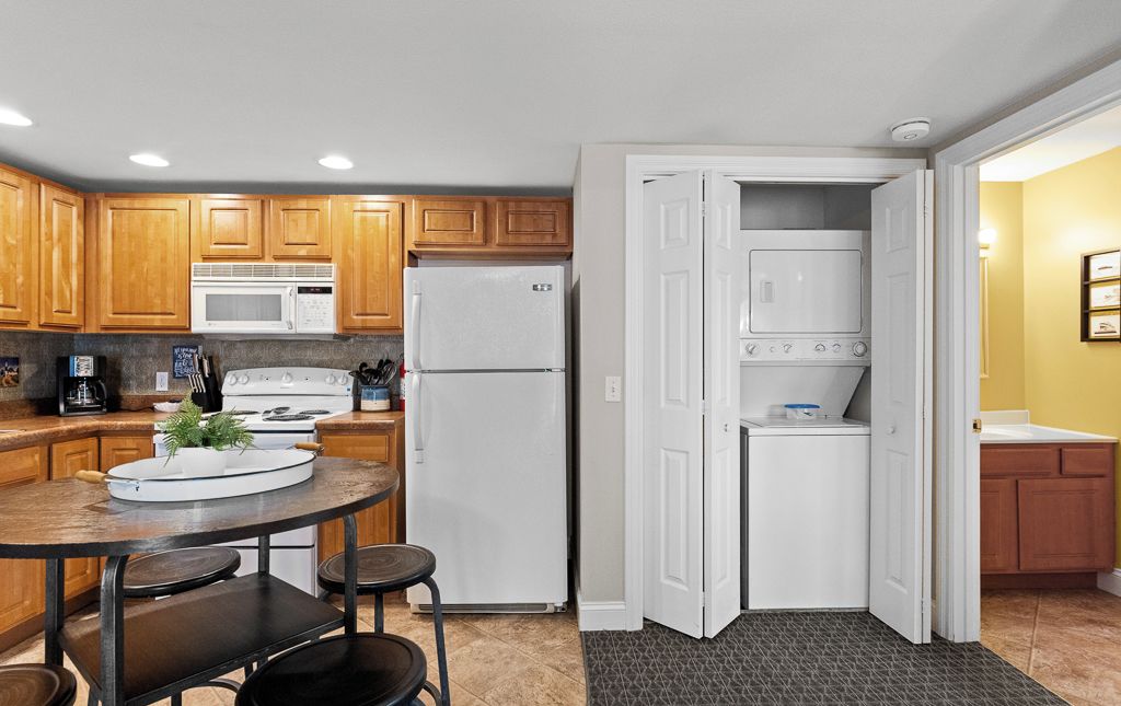 A compact kitchen with wooden cabinets, a white refrigerator, a microwave, and a stove. There is a small dining area with a table and chairs.