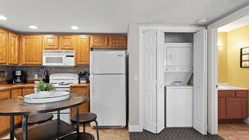 A compact kitchen with wooden cabinets, a white refrigerator, a microwave, and a stove. There is a small dining area with a table and chairs.