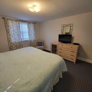 Een slaapkamer met een bed, een dressoir, een televisie en een raam met gordijnen.