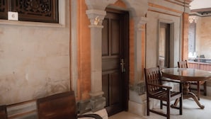 A dining area with a round table and chairs, a wooden door, and stone walls. - Pande Permai Guest House (Ubud)