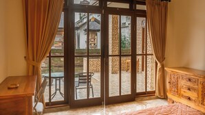 A room with a sliding glass door leading to an outdoor patio, a wooden dresser, and a bed. - Pande Permai Guest House (Ubud)