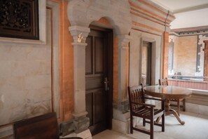 A room with a wooden door, a round table with chairs, and a window with a view. - Pande Permai Guest House (Ubud)