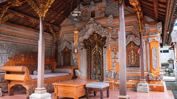 An ornate room with a large wooden bed, a bench, and a small table. - Pande Permai Guest House (Ubud)