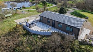 Una casa moderna con un patio, un estanque y autocaravanas al fondo.