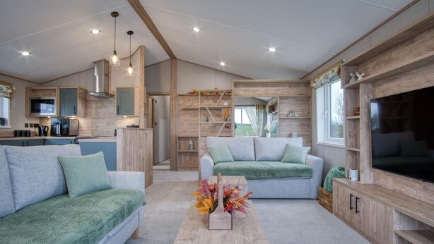 Una sala moderna con un sofá, una mesa de centro con un arreglo floral, un televisor y una cocina con armarios de madera y un microondas.