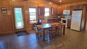 A wooden cabin-style kitchen with a dining table, chairs, a refrigerator, a microwave, and a sink. - Lake Superior Log Cabin - Wake up to Waves! (Lutsen)