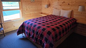 A wooden cabin room with a bed, two bedside lamps, a window, and a small table. - Lake Superior Log Cabin - Wake up to Waves! (Lutsen)