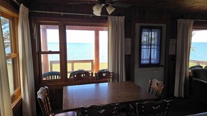 A wooden cabin with a dining table and chairs, large windows with curtains, and a view of the sea. - Lake Superior Log Cabin - Wave Watching Delight! (Lutsen)