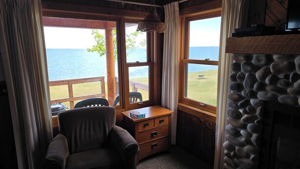 A cozy room with a view of the water, a stone fireplace, and a wooden desk with a chair. - Lake Superior Log Cabin - Wave Watching Delight! (Lutsen)