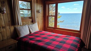 A wooden cabin room with a bed, two windows, and a view of the ocean. - Lake Superior Log Cabin - Wave Watching Delight! (Lutsen)