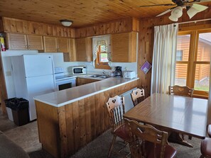 A wooden cabin kitchen with a refrigerator, microwave, stove, sink, and wooden dining table with chairs. - Lake Superior Log Cabin - Wave Watching Delight! (Lutsen)