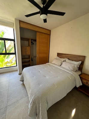 Une chambre à coucher avec un lit, un ventilateur de plafond, une armoire et une vue sur la verdure.