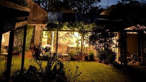 Ein Haus mit einem großen Baum im Garten, einer überdachten Terrasse und einem gut beleuchteten Innenraum.