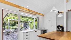 Eine moderne Küche mit weißen Schränken, einer Holz Arbeitsplatte und Blick auf einen Garten durch große Fenster.