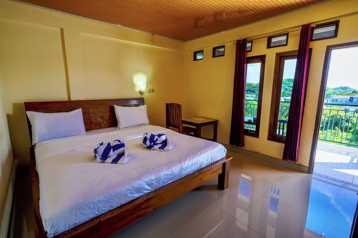Une chambre d’hôtel avec un grand lit, une table de chevet, une chaise et une vue sur la verdure par les fenêtres.