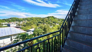 A staircase with a metal railing, leading to a balcony overlooking a lush green hillside with buildings in the distance. - Golo Tango Homestay (Labuan Bajo)
