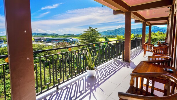 A balcony with a view of a river and mountains, wooden furniture, and a potted plant. - Golo Tango Homestay (Labuan Bajo)