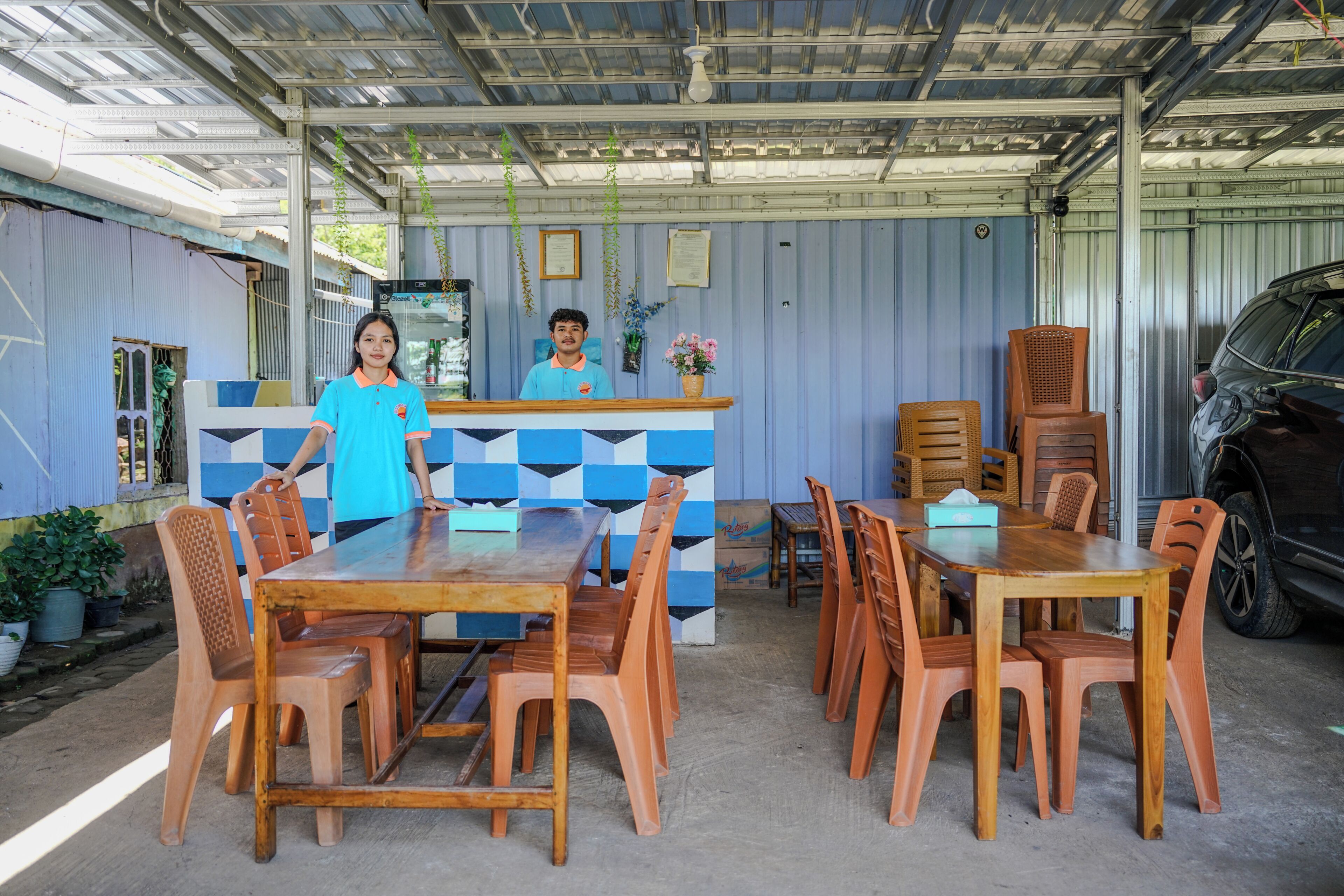 A covered outdoor dining area with a counter, wooden tables, and chairs.
