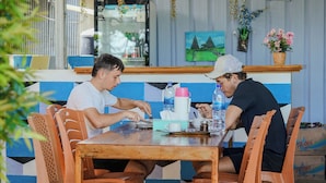 A wooden table with chairs, a refrigerator with beverages, and a painting on the wall. - Golo Tango Homestay (Labuan Bajo)