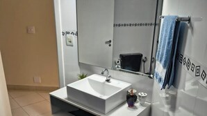 Een moderne badkamer met een witte wastafel, een grote spiegel en een handdoekhouder.