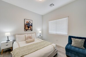 A bedroom with a bed, bedside tables, a lamp, a window with blinds, a blue sofa, and a wall-mounted artwork. - Comfy Stay7 Beds| Close to Strip & Attraction (Enterprise)