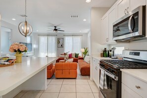 A modern kitchen with a central island, a dining area with orange furniture, and a living room with a sofa and curtains. - Comfy Stay7 Beds| Close to Strip & Attraction (Enterprise)