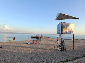 A pebbled beach with a signboard, a bicycle, and people relaxing.