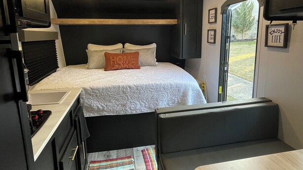 A compact RV interior with a kitchenette, a bed with pillows, a bench, and a small table. - Welcome to Cozy by the Coast! Just steps from the beach, ocean is calling you! (Surfside Beach)